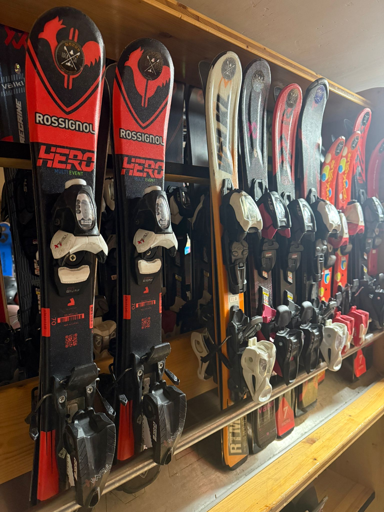 Alignement de skis Rossignol Hero rouges et noirs sur un râtelier en bois chez Loca'ski