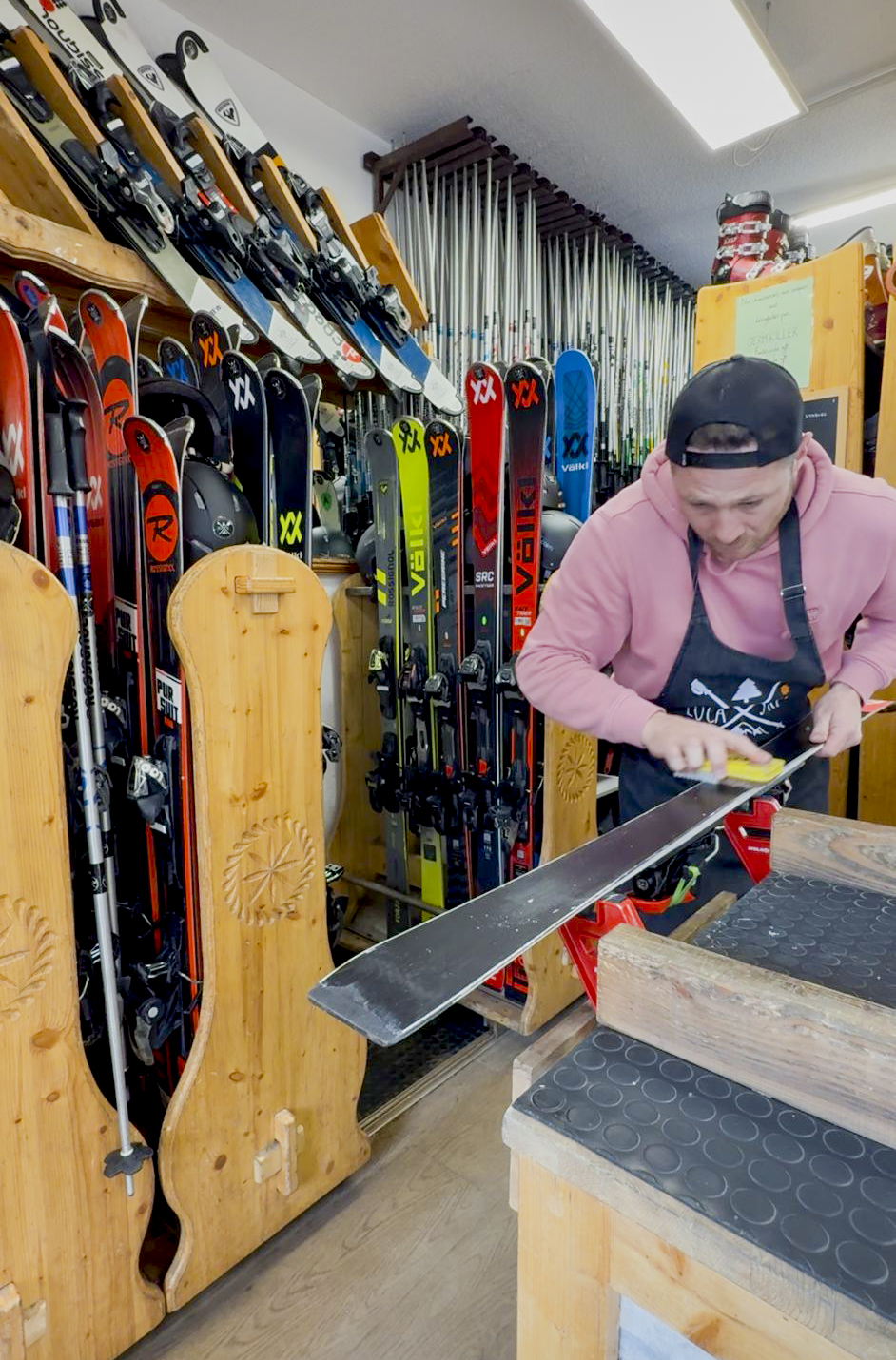 Technicien de ski effectuant le fartage manuel d'un ski alpin dans un atelier de réparation professionnel.