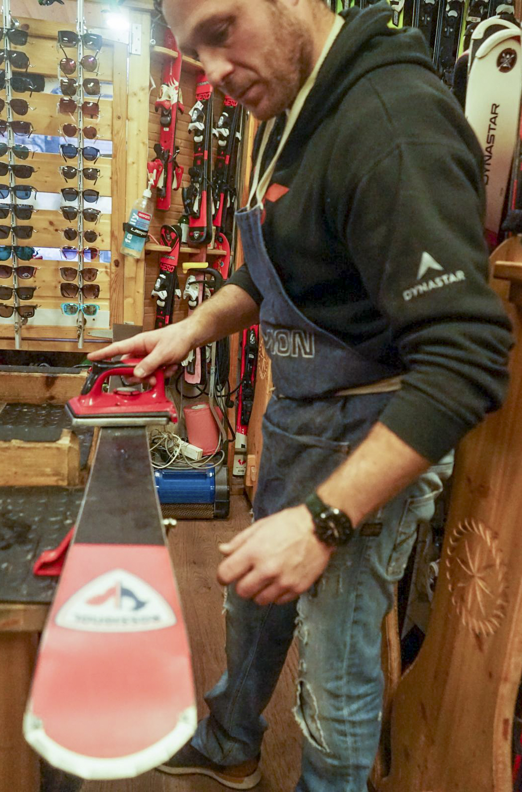 Un technicien entretient un ski en utilisant un fer à farter rouge dans un atelier de sports d'hiver.
